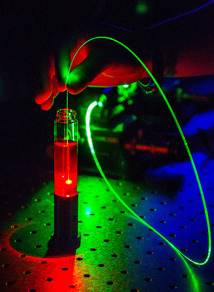 This image shows a number of optical phenomena, starting with a green laser (532-nm Nd:YAG) guided by a multimode silica optical fiber to a vial containing an organic dye