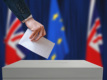 hand putting ballot in box, with U.K. and EU flags in background