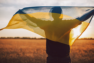 Man with Ukranian flag facing field at sunset